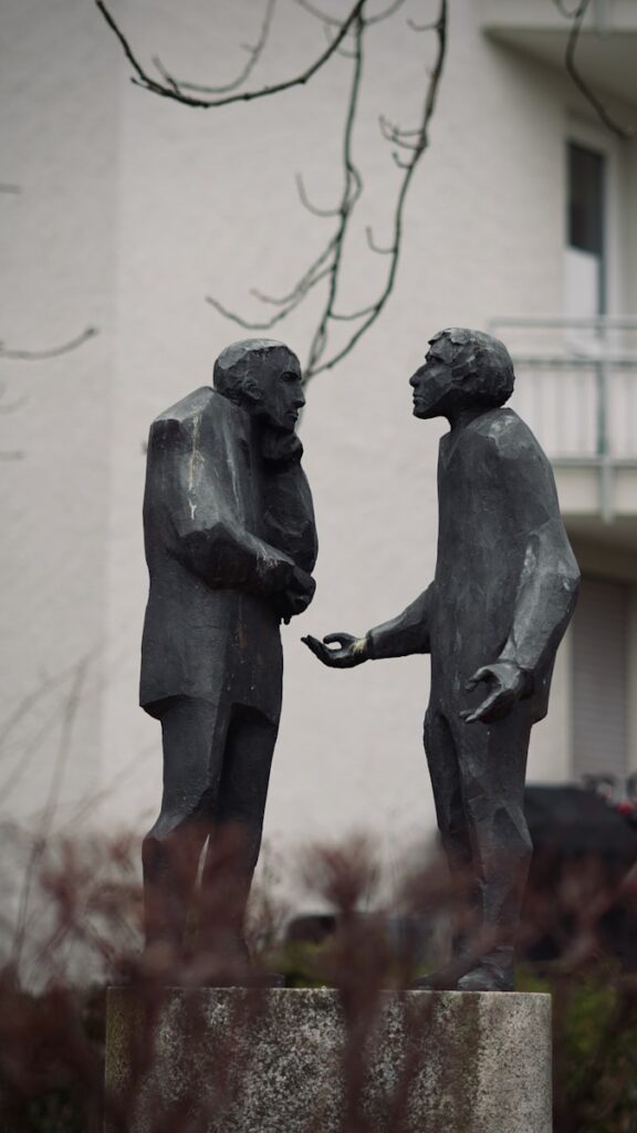 Two abstract figures in conversation on a pedestal.
